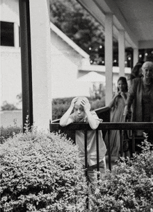 a black and white photo of a young boy leaning on a railing with his hands on his head