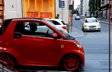 a red car is driving down a street with a taxi sign in the background