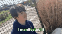 a boy is standing in front of a fence with the words " i manifested it " written on it