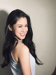 a woman with long black hair wearing a white tank top smiles