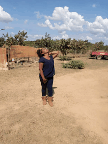 a woman stands in a dirt field with a red honda truck in the background