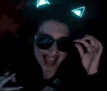 a woman wearing sunglasses and headphones with cat ears on her head is smiling in the dark .