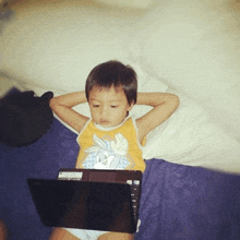 a young boy is laying on a bed using a laptop computer