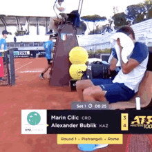 a man sits on a chair with a towel on his face during a tennis match between marin cilic and alexander bublik