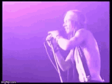 a man is singing into a microphone on a stage in a purple light .