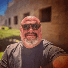 a bald man with a beard wearing sunglasses and a black shirt is taking a selfie .