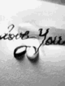 a black and white photo of a person 's hand writing i love you on a piece of paper .