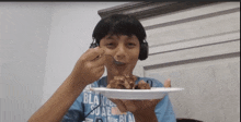 a boy wearing headphones is eating a piece of cake from a white plate