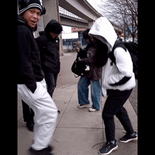 a group of people standing on a sidewalk with one wearing a hoodie that says ' abercrombie & fitch '