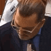 a man in a suit and tie is wearing glasses and looking down .
