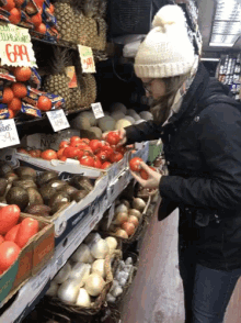 a woman is looking at tomatoes in a grocery store with a sign that says " tomatoes " on it