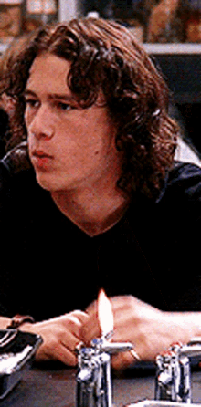 a young man with curly hair is sitting at a table with a lit candle in front of him .