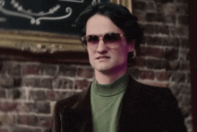 a man wearing sunglasses is standing in front of a brick wall
