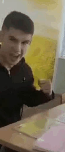 a young man is sitting at a desk in a classroom holding a book .