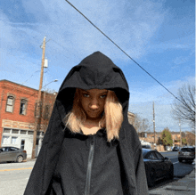 a woman wearing a black jacket with a hood is standing on a street