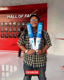 a man in a plaid shirt is holding a pair of balloons in front of a hall of fame wall