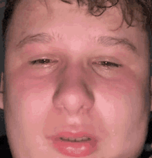 a close up of a young man 's face with a red face and tears coming out of his eyes .