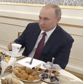 a man in a suit and tie is sitting at a table with food