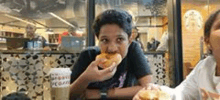 a boy is eating a donut in a restaurant while sitting at a table .