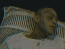 a man with a tattoo on his face is sleeping in a bed .