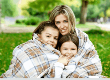 a woman and two young girls wrapped in a plaid blanket