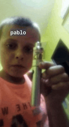 a young boy in a pink shirt is holding an electronic cigarette with pablo written on his face