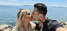 a man and a woman kissing in front of the ocean wearing face masks