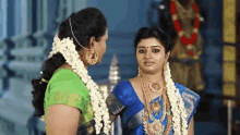 two women are standing next to each other in a temple . one of the women is wearing a blue saree .