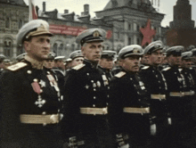 a group of men in military uniforms stand in front of a building with a red star in the background