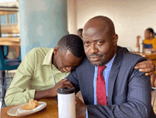 a man in a suit and tie is sitting next to another man at a table .