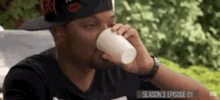 a man wearing a hat is drinking from a cup .