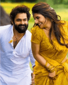 a man with a beard and a woman in a yellow saree are holding hands and smiling .