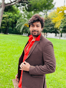 a man in a brown jacket and red shirt stands in a park