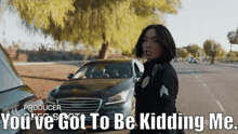 a woman in a police uniform is standing in front of a black car and says " you 've got to be kidding me "