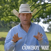 a man wearing a cowboy hat and a blue shirt is standing in front of a sign that says " the cowboy way "