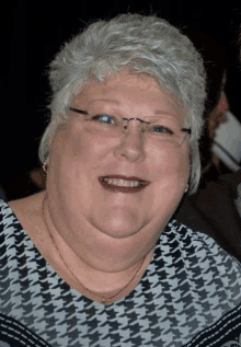 a woman wearing glasses and a plaid shirt is smiling for the camera