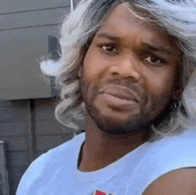 a man with a beard and gray hair is wearing a white tank top and a wig .