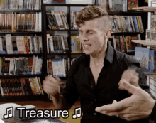 a man in a black shirt is sitting in front of a bookshelf with the word treasure written on the bottom