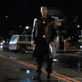 a man in a trench coat is dancing on a street at night ..