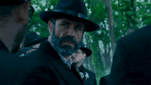 a man with a beard wearing a hat and a suit says the real game begins now