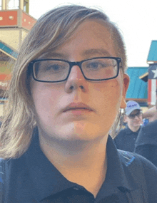 a young woman wearing glasses and a black shirt looks at the camera in front of a carnival ride