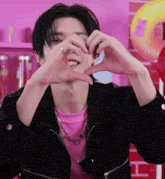 a young man making a heart with his hands in front of a pink background