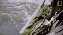 a person is standing on a rock near a body of water with a national geographic logo in the corner