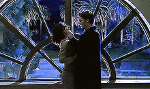 a man and a woman are hugging in front of a window with palm trees in the background