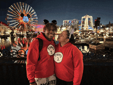 a man and woman wearing thing 1 and thing 2 hoodies pose for a picture in front of a ferris wheel