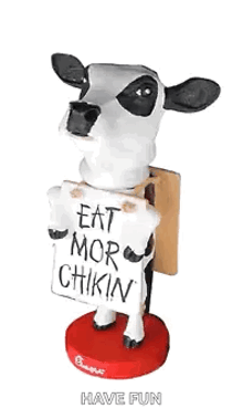 a cow bobble head holding a sign that says eat more chikin .