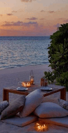 a table with plates and candles on it is sitting on the beach near the ocean at sunset .