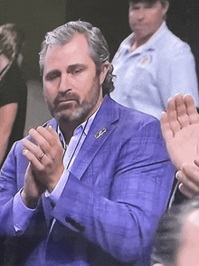 a man in a blue suit applauds while wearing a ring on his finger