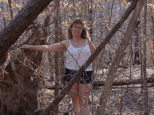 a woman in a white tank top and shorts is standing in the woods