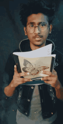 a young man with glasses is holding a book with a butterfly on it